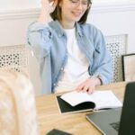 Smiling woman in casual attire working at home office with a laptop and notebook.