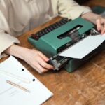 Close-up of hands using a vintage typewriter, with paper and script on a wooden desk.